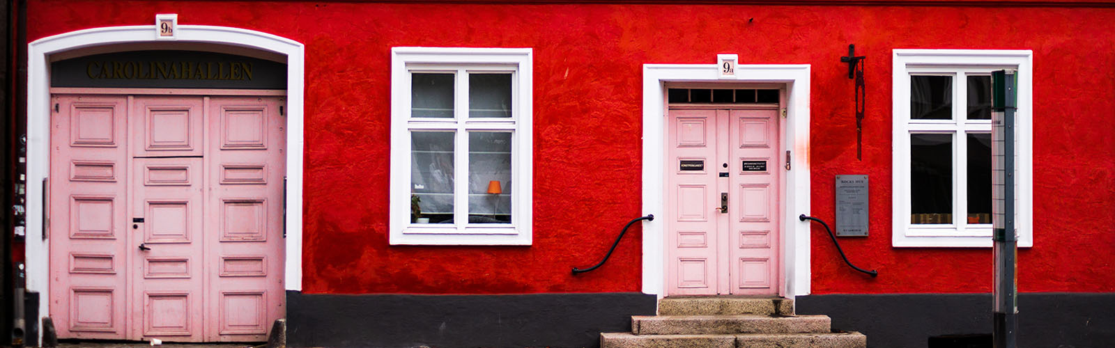 A close-up of the first story of a red building with two windows and two pink doors.